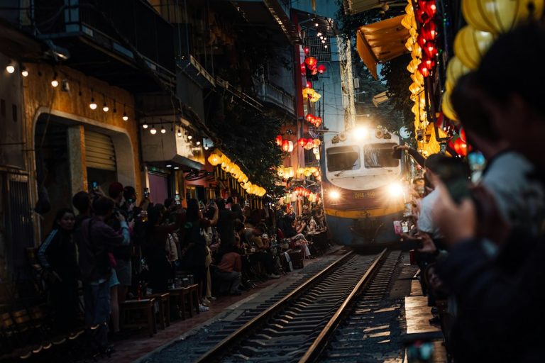 Train passing through Hanoi Train Street with visitors beside the railway